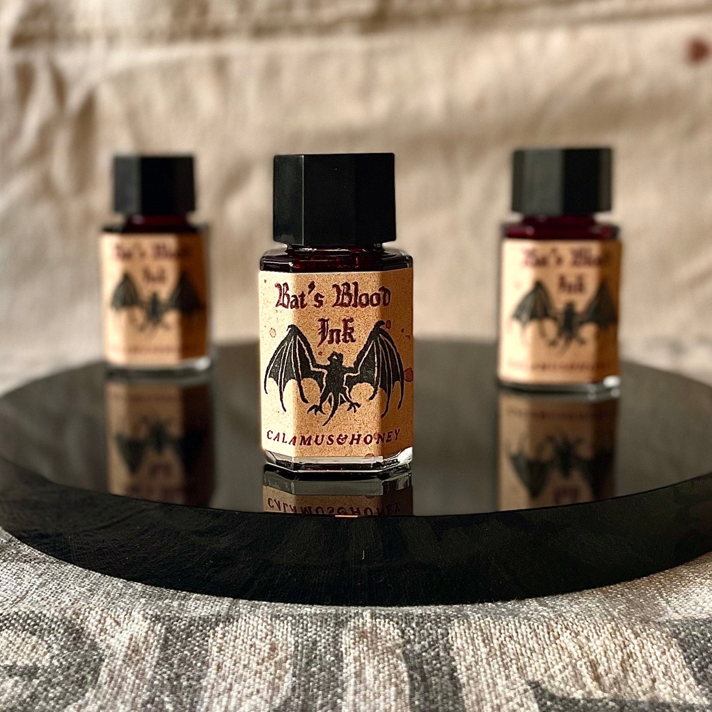 Three bottles of 'Bat's Blood Ink' on a black tray with a textured background